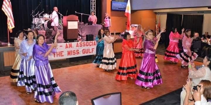 A group of performers in colorful dresses dancing during a community festival program.