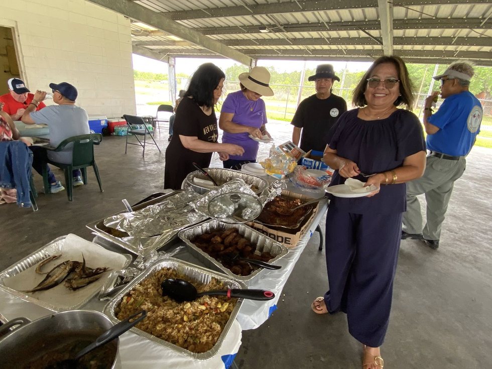 A buffet table with prepared dishes at an outdoor Filipino-American community gathering.