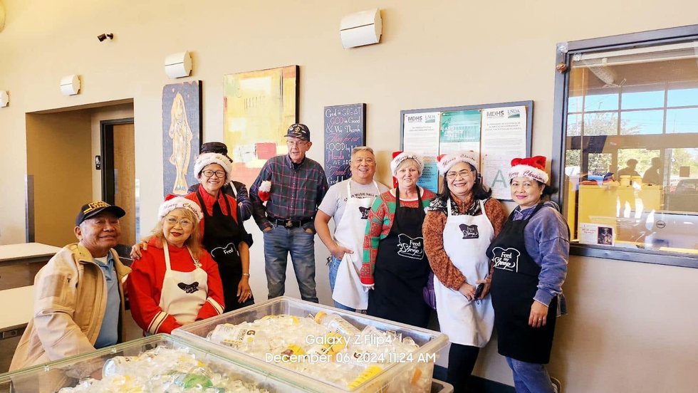 Volunteers gathered behind tables of food and supplies during a service activity.